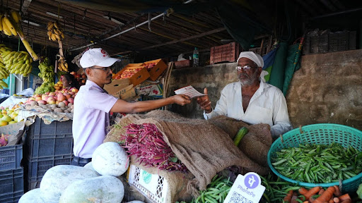 An M.I.O. volunteer hands cancer awareness literature to a local vegetable vendor during the Koppa rally