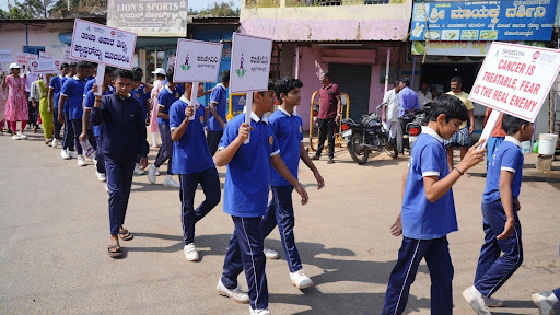 School students march alongside M.I.O. volunteers in Ranebennur, holding placards that read "Cancer is Treatable, Fear is the Real Enemy"