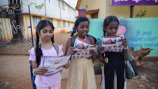 Young students outside a Shikaripura school pause to read M.I.O. cancer awareness pamphlets